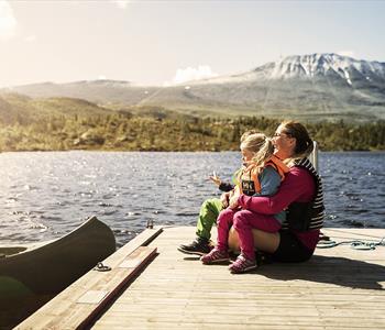 Mor og datter sitter ved innsjøen foran Gaustatoppen i Telemark