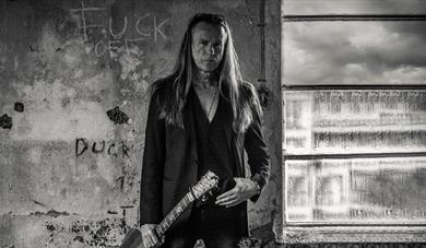 mann med langt blondt hår , sort jakke og gitar,