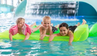 3 children lying on an air mattress in the pool of the bathing park