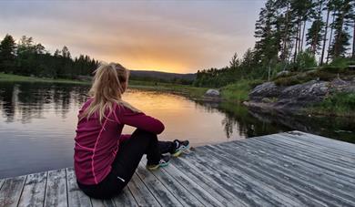 girl sitting on a wharf and looking out at the water Lille Nakksjø cabin farm in Villmarkseventyret