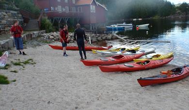 Kanoer som ligger på en strand og noen mennesker