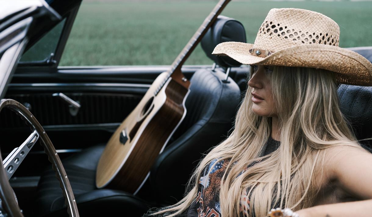 blond dame med langt hår, i cabriolet og gitar