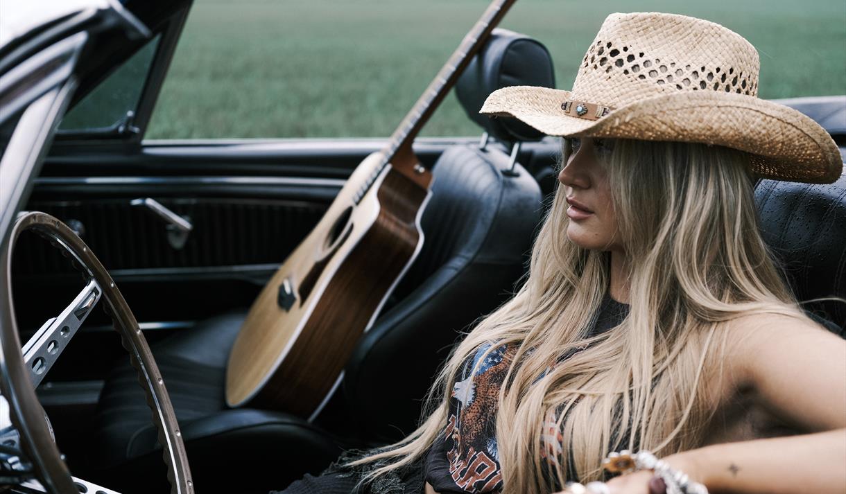 blond dame med langt hår, i cabriolet og gitar