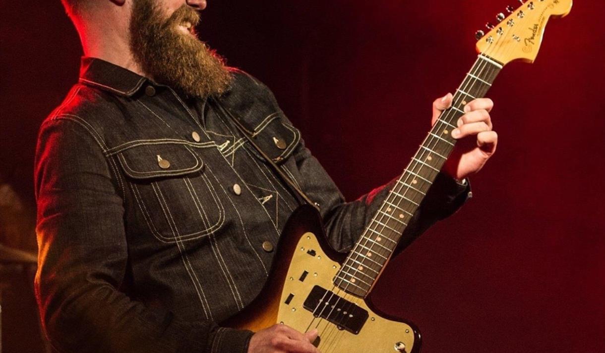 mann med langt skjegg og gitar med sort og dus rødfage