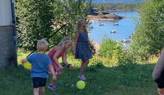 Fra Sanglek for Barn 2022. Bilde viser små barn som leker seg på gresset med et vann i bakgrunnen