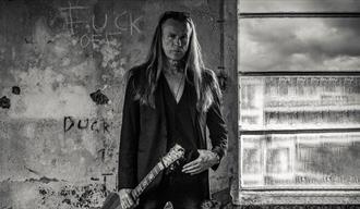 mann med langt blondt hår , sort jakke og gitar,