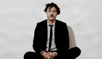 bilde av Bjørn Tomren, sittende med bena i kryss, sort dress og slips