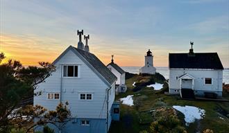 hvite hus med fyrhus i bakgrunn, gul oransje himmel