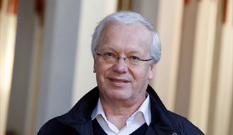 gråhåret mann med briller, blå jakke og hvit skjorte