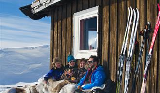 2 par som sitter foran hytten på vinter og nyter solen