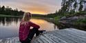 girl sitting on a wharf and looking out at the water Lille Nakksjø cabin farm in Villmarkseventyret