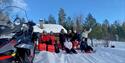 group sitting in the snow behind a snowmobile