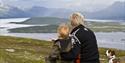 adult and child with dog sitting and looking out over the landscape