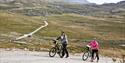 older couple pushing their bikes and Gaustatoppen in the background