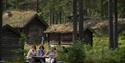 tre damer drikker kaffe, gamle hus og stabbur i skog