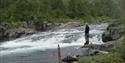 man standing by a river fishing