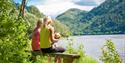 2 ladies with a small dog sit on a bench and look out over the water