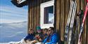 2 couples sitting in front of the cabin in winter enjoying the sun