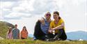 couple sitting on the ground and smiling 2 girls and a boy standing in the background