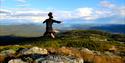 Photo from one of Lifjell's many summits. Blue sky, beautiful view of lake Norsjø and Telemark, and a girl jumping high in the air.