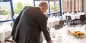 man arranges cutlery on a nice covered table