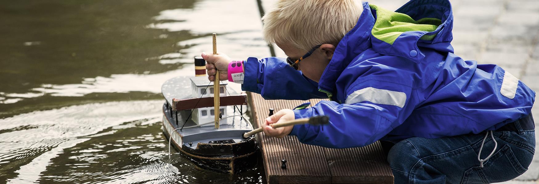 Boy sails his boat on the Telemark Canal model at the canal park at Vest-Telemark Museum in Eidsborg