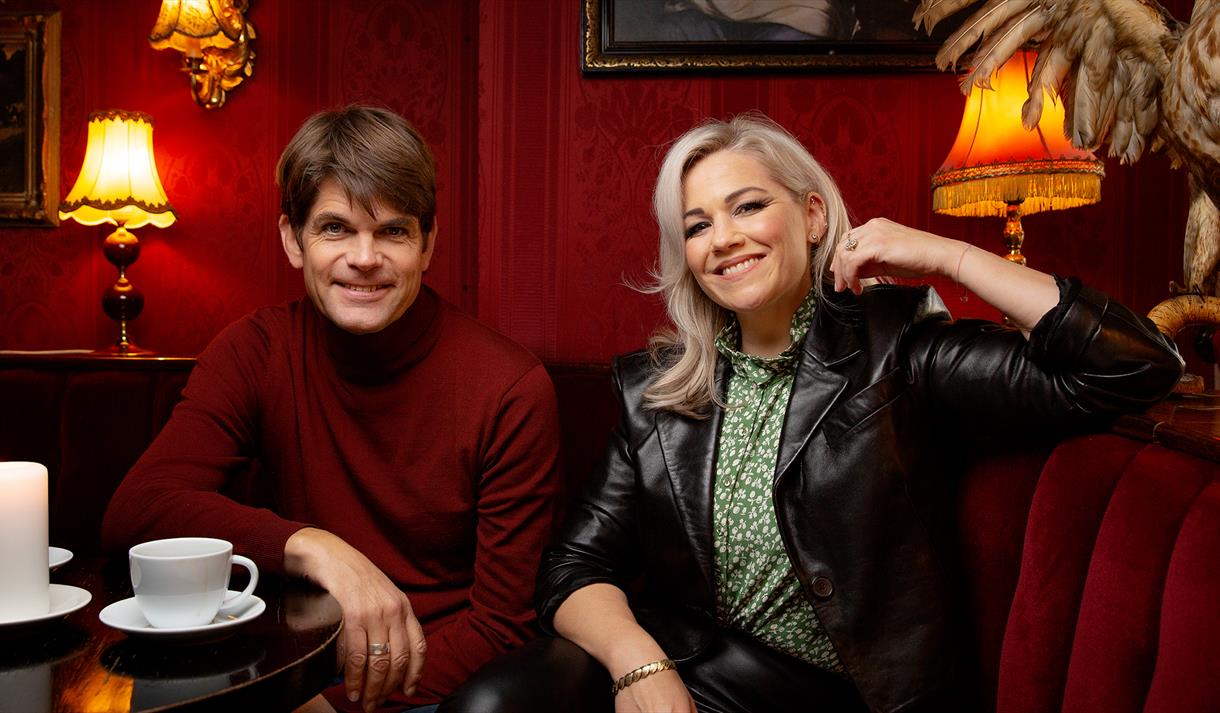 Lars Bremnes og Maria Haukaas Mittet sitter i en rød sofa med kaffekoppene foran seg