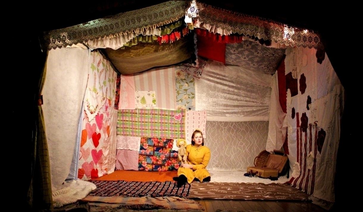 Barneforestillingen LILLE: En jente sitter inne i et hus som er bygget av gamle duker og gardiner