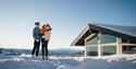 par med barn står foran en hytte på Lifjell Tunet om vinteren
