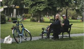 kvinne og mann sitter på en parkbenk og ved siden står en blå sykkel