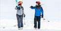 mann og kvinne går med ski over skuldra