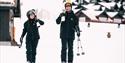 mann og kvinne bærer skiene langs hyttene på Raulandskisenter