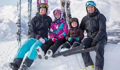 family sitting on a pile of snow with their skiers standing behind them