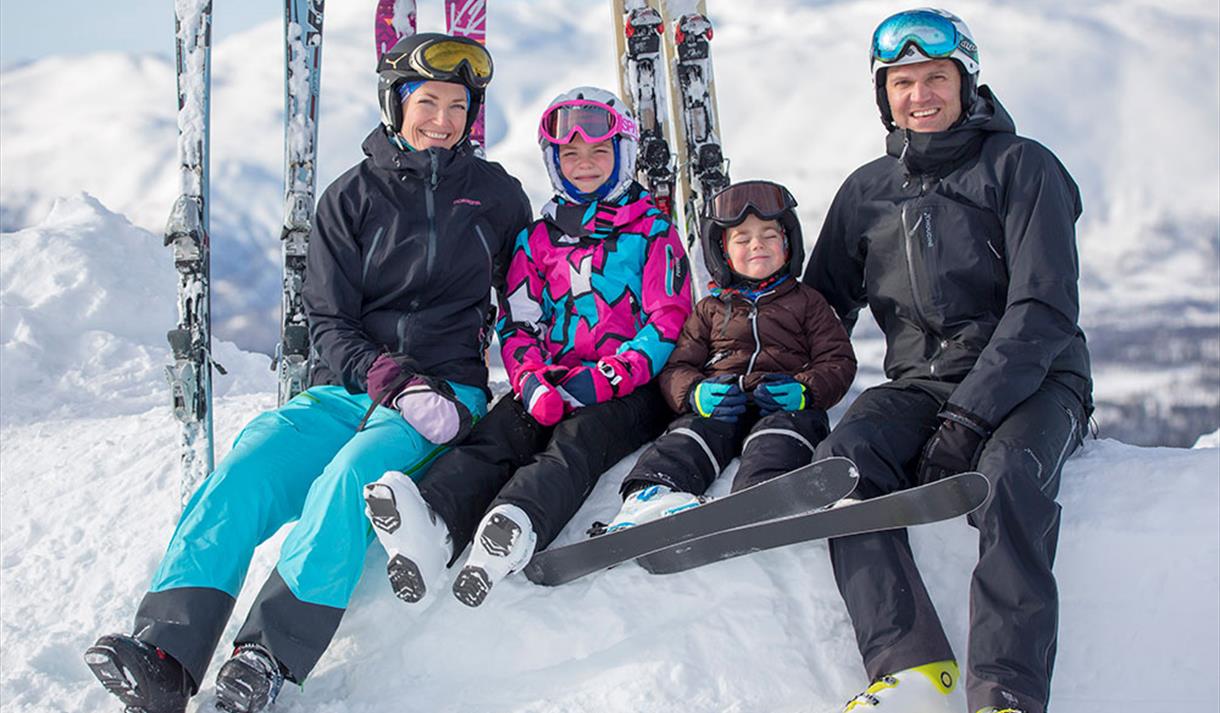family sitting on a pile of snow with their skiers standing behind them
