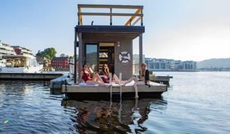 Saunaboat Melvin I Porsgrunn. Bilde av saunabåten ved bryggekanten i Porsgrunn med 3 jenter som ligger og soler seg foran på dekket