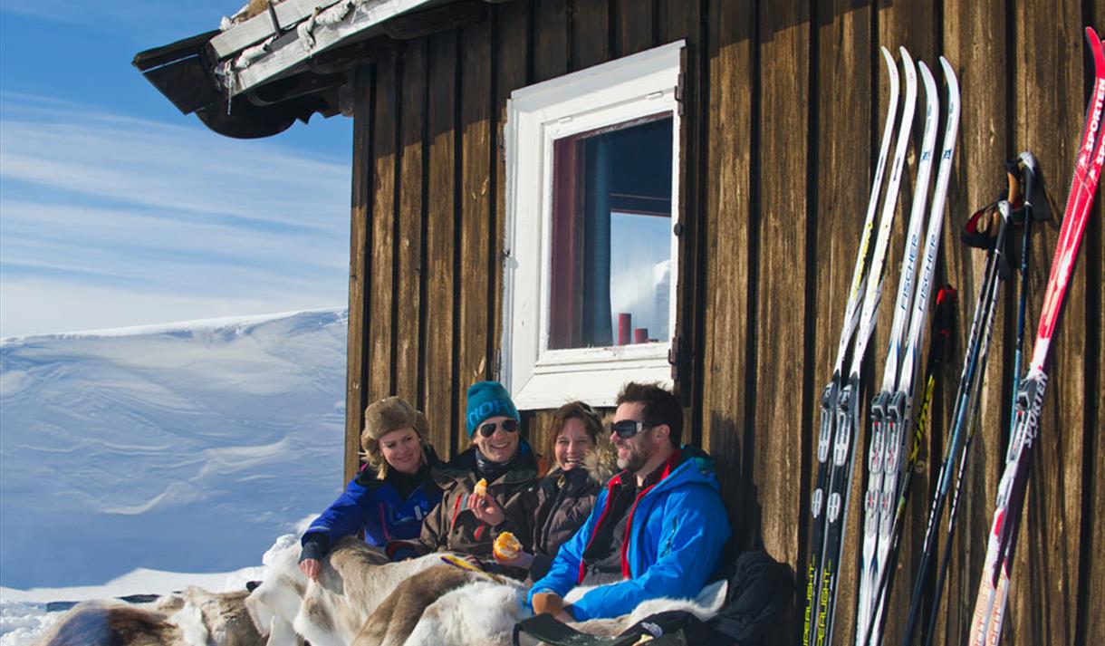 2 couples sitting in front of the cabin in winter enjoying the sun