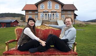 kunstnerparet Elisabeth de Lunde og Jakob Zethners sittende på en sofa foran  Villa Lunde