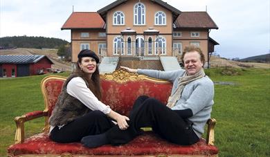 the artist couple Elisabeth de Lunde and Jakob Zethners sitting on a sofa in front of Villa Lunde
