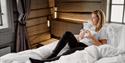 dame sitter på senga med en kopp kaffe på Tollboden Hotell og Restaurant i Kragerø