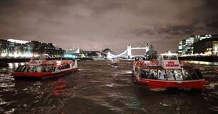 City cruises boats at night in front of Tower Bridge