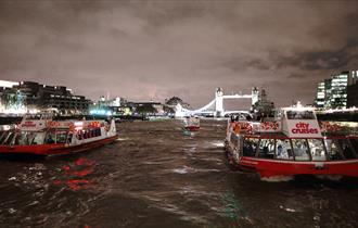 City cruises boats at night in front of Tower Bridge