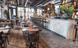 The restaurant has modern oak floors next to patterned floor tiles. The tables are simple wooden tables with chairs, surrounded by warehouse style dec