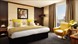 A hotel room featuring a double bed with a yellow chair and a vase filled with beautiful flowers.