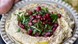 A bowl of hummus with pomegranate on top.