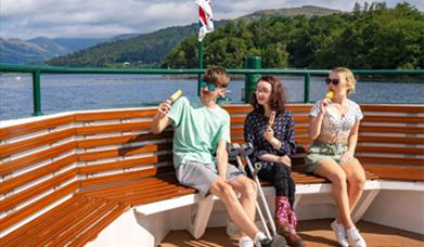 three people, one using crutches sat on decking eating ice cream in the sunshine