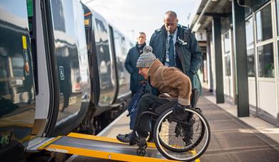 Person in a wheelchair boarding a GWR train via the ramp with station staff assisting