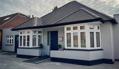 Entry to AbleStay, a grey bungalow style building with a wheelchair ramp leading up to the front door