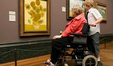 Person in a wheelchair with a companion looking at van gough's sunflowers at The National Gallery Trafalgar Square