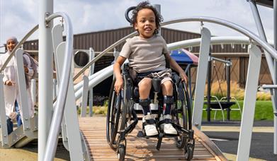 Child in a wheelchair on an accessible playground ramp.