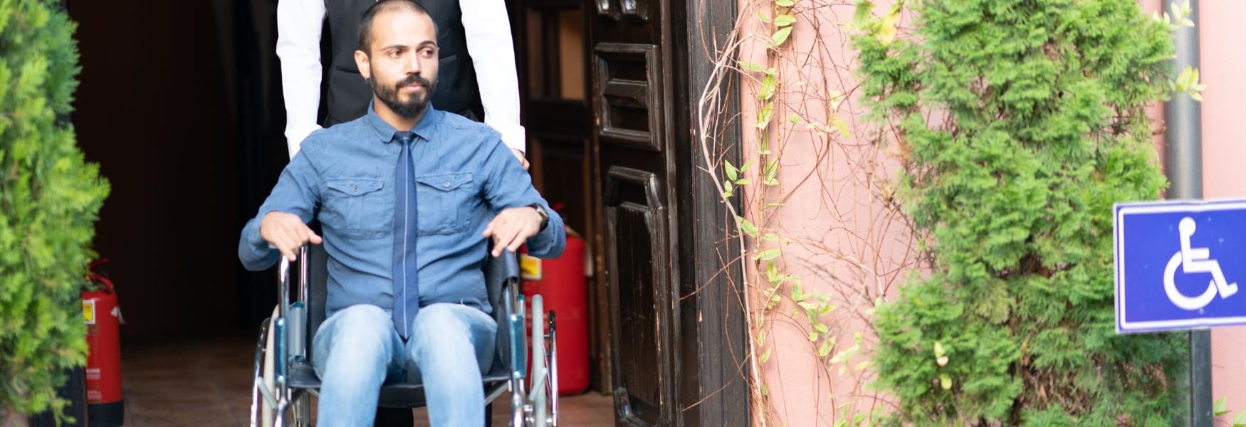 A man in a wheelchair being pushed through a hotel entrance by a receptionist